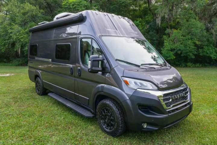 Gray RV rental camper van with off-road tires and awning, parked on green grass, ready for adventure.. Noovo Noovo Class B 2026