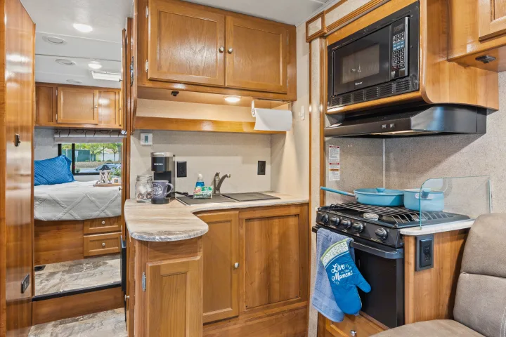 RV rental interior: a functional kitchen with microwave, stove, sink, coffee maker, and a peek into the bedroom.. Coachmen Leprechaun 2019