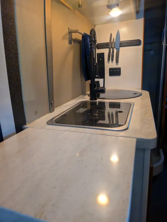 Modern RV rental kitchenette featuring a light-colored countertop, sink, covered stove, and magnetic knife strip.. Winnebago Travato 2018