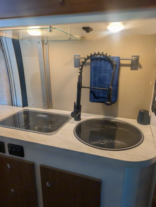Compact rv rental kitchen with an integrated stovetop, sink, pull-down faucet, under-cabinet lighting, and wooden storage.. Winnebago Travato 2018