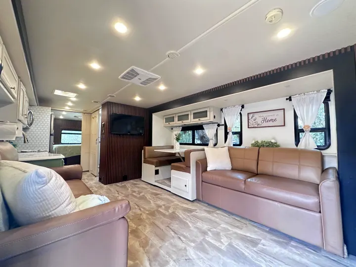 Modern rv rental living area features brown sofas, dining booth, kitchen view, and hallway leading to a rear bedroom.. Fleetwood Flair 2021