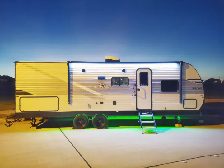 A modern Jayco travel trailer, ideal for an rv rental, stands illuminated at dusk with vibrant green underglow and bright awning lights.. Jayco Jay Flight SLX 2025