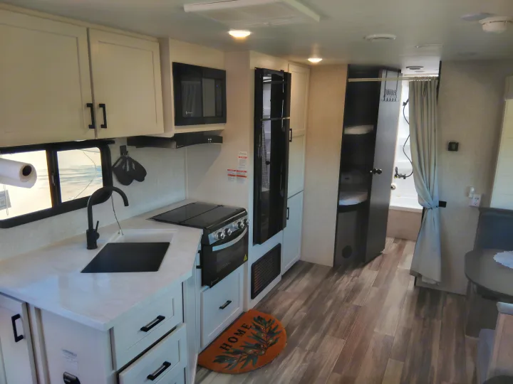 Modern RV rental interior featuring a full kitchen with microwave, stove, sink, and fridge, plus a compact dining area and bathroom.. Jayco Jay Flight SLX 2025