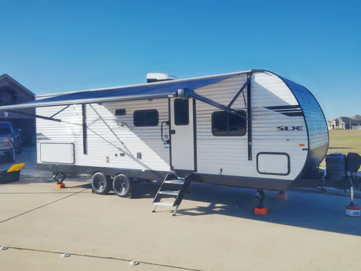 RV rental: A white Jay Flight travel trailer with an extended awning, parked on a concrete drive under a clear blue sky.. Jayco Jay Flight SLX 2025