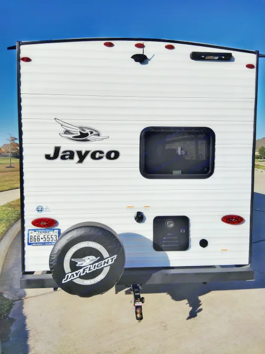 Rear view of a white Jayco travel trailer, ideal for an rv rental. Shows a spare tire and Texas license plate.. Jayco Jay Flight SLX 2025