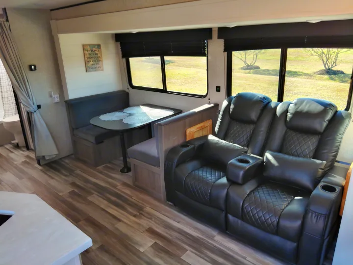 This RV rental interior features a comfy reclining sofa, dinette booth, and scenic windows overlooking nature.. Jayco Jay Flight SLX 2025