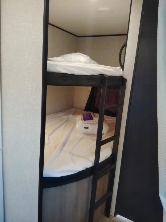 RV rental bunk beds, neatly prepared with white sheets & packaged pillows. A ladder is visible for top bunk access.. Jayco Jay Flight SLX 2025