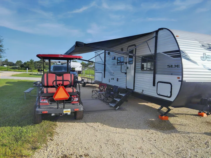 RV rental adventure! A travel trailer with an awning and a red golf cart parked at a sunny campsite.. Jayco Jay Flight SLX 2025