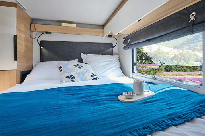 Experience comfort in this RV rental bedroom: cozy bed, reading lights, and a window overlooking a vibrant lavender field.. Pilote A630G 2026