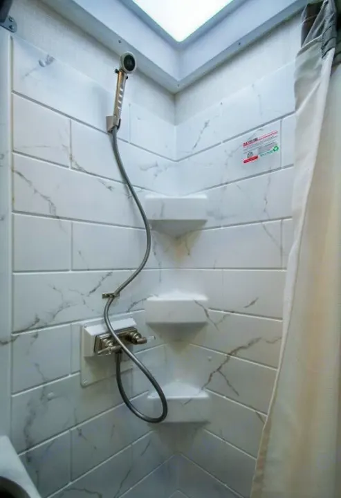 RV rental shower: White faux-marble tiled stall with handheld shower, controls, corner shelves, and a skylight above.. Axis 24.1 2027