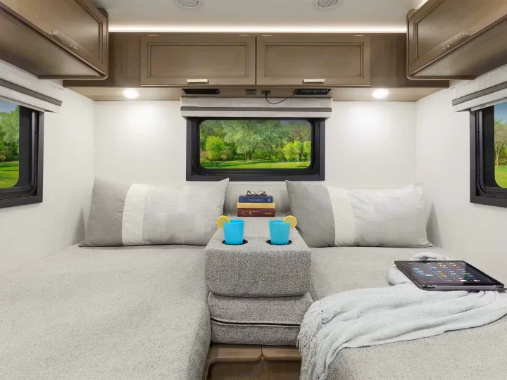 Cozy RV rental interior featuring a versatile seating/bed area with cushions, overhead storage, a scenic window, and a tablet.. Axis 24.1 2027