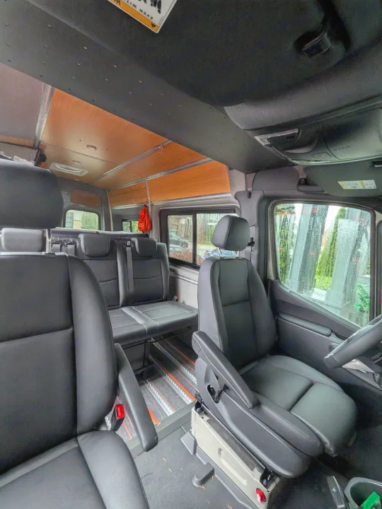 Inside an RV rental: versatile van interior with black leather seating, movable floor tracks, and cozy wood ceiling.. Mercedes-Benz Sprinter 2025