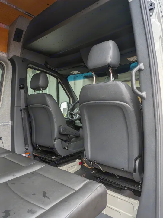 View inside an RV rental: front driver/passenger seats, steering wheel, and custom ceiling with wood and fabric paneling.. Mercedes-Benz Sprinter 2025