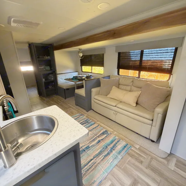 Inside this modern RV rental, find a comfortable living space with a kitchen, dining booth, sofa, and scenic window views.. Forest River Tracer Ultra Lite LE 2025