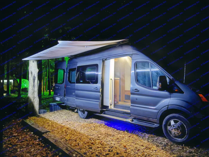 Night camping in a modern rv rental camper van with an extended awning, open door, and blue underglow lighting. Cozy interior visible.. Coachmen Beyond 22C 2020