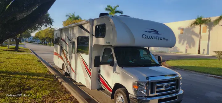 White Quantum SE Class C RV rental parked on a sunny day with palm trees and a road in the background.. Thor Quantum 2021