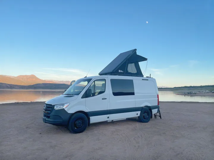 This white Mercedes Sprinter RV rental features a pop-top tent, ideal for lakeside camping and van life under the moonlit sky.. Mercedes Sprinter 2024