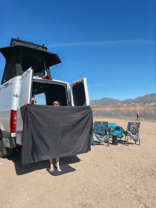 This rv rental offers a private outdoor shower setup by the lake, perfect for van life amidst mountains under a clear sky.. Mercedes Sprinter 2024