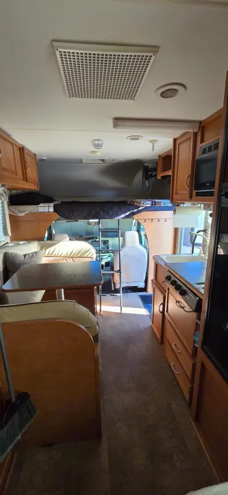 Spacious RV rental interior featuring a kitchen, dining booth, and cab-over bunk bed. Wooden cabinets and light flooring visible.. Winnebago Minnie Winnie 2019