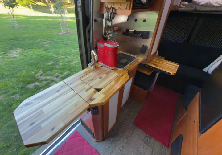 RV rental camper van kitchen: wooden counter with sink, red coffee maker, extendable counter, & view of green grass.. Roadtrek Simplicity SRT 2019