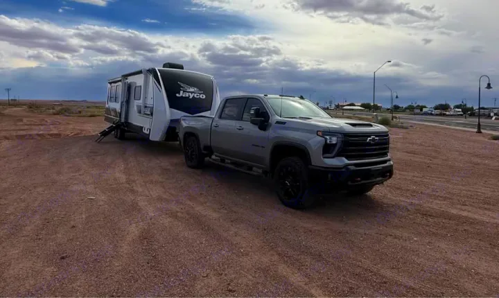 A gray pickup truck tows a white Jayco RV on a dirt lot. Get ready for an RV rental adventure with this perfect setup!. Jayco Eagle 2024
