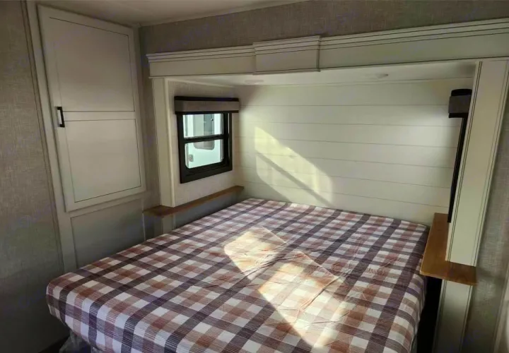 Inviting RV rental bedroom with a checkered bed, shiplap wall, window, and built-in storage cabinet.. Jayco Eagle 2024