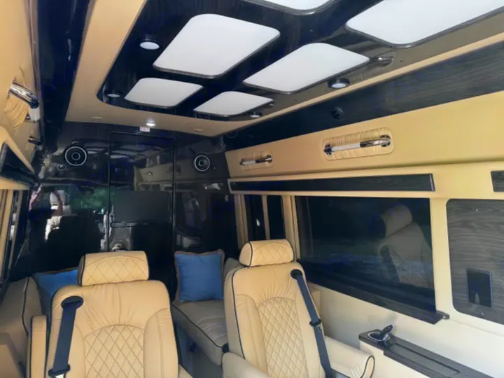 Luxurious RV rental interior, featuring plush beige quilted seats, elegant dark wood trim, bright ceiling lights, and a TV for premium travel comfort.. Ultimate Toys Ultimate Coach 2024