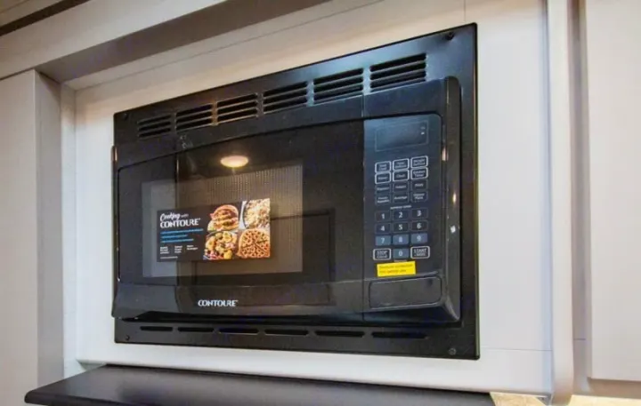 Built-in black Contoure microwave appliance in an RV rental kitchen, ready for convenient cooking. Features a display sticker of food.. Four Winds 28z 2027