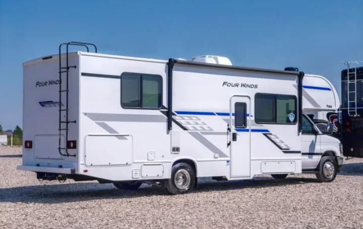 This white Four Winds Class C RV rental is parked on a gravel lot, ready for adventure under a clear sky.. Four Winds 28z 2027