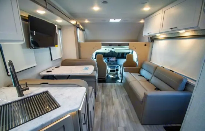 Spacious, modern rv rental interior featuring a kitchen, dining booth, sofa, TV, and driver's cabin view.. Four Winds 28z 2027