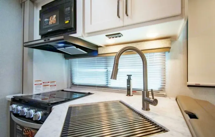 A well-equipped modern RV rental kitchen features a microwave, cooktop, sink with drying rack, and white cabinets.. Four Winds 28z 2027