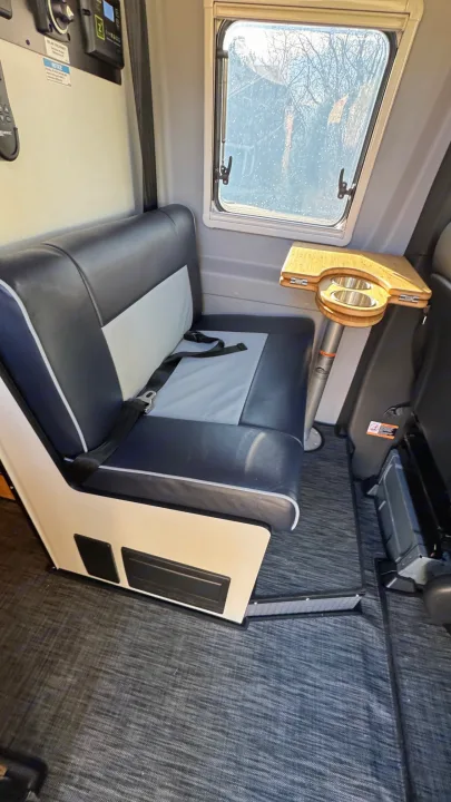 RV rental interior features a cozy blue and gray dinette, a wooden table with cup holders, and a clear window view.. Winnebago Revel 2023