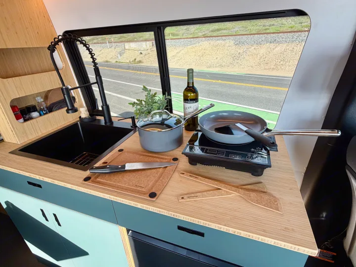 Well-equipped RV rental kitchen featuring a sink, induction cooktop, and cookware, ideal for cooking while traveling.. Mercedes-Benz Sprinter 2025