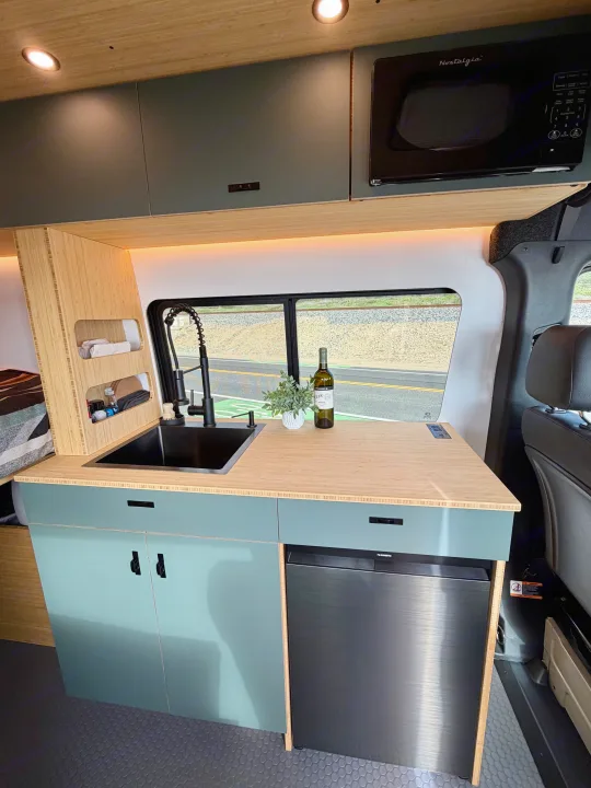 Modern RV rental kitchen with sink, microwave, fridge, and stylish teal cabinets for comfortable travel.. Mercedes-Benz Sprinter 2025