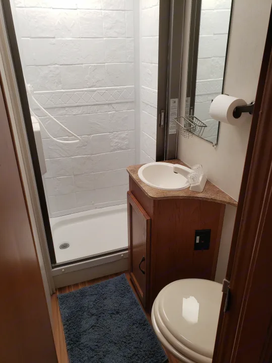 Compact RV rental bathroom: shower, sink, and toilet, with white textured walls and a wooden vanity.. Coachmen Freelander 2013
