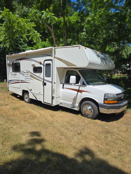 White Coachmen Freelander RV rental, parked on sunlit grass with lush green trees in the background.. Coachmen Freelander 2013