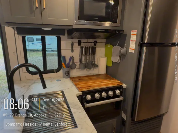 Inside a Fireside **rv rental**, a well-equipped **RV kitchen** with a sink, microwave, stove, and refrigerator in Apopka, FL.. Keystone Bullet 2022