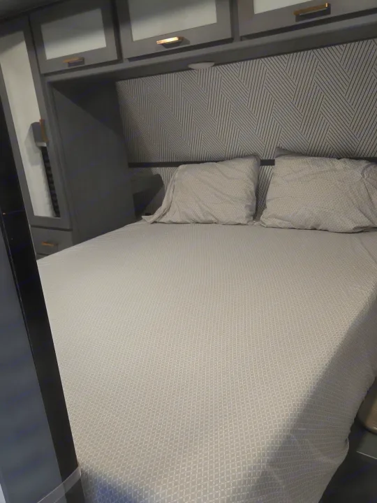 Modern RV rental: a compact bedroom features grey bedding, a geometric headboard, and sleek overhead cabinets.. Keystone Bullet 2022