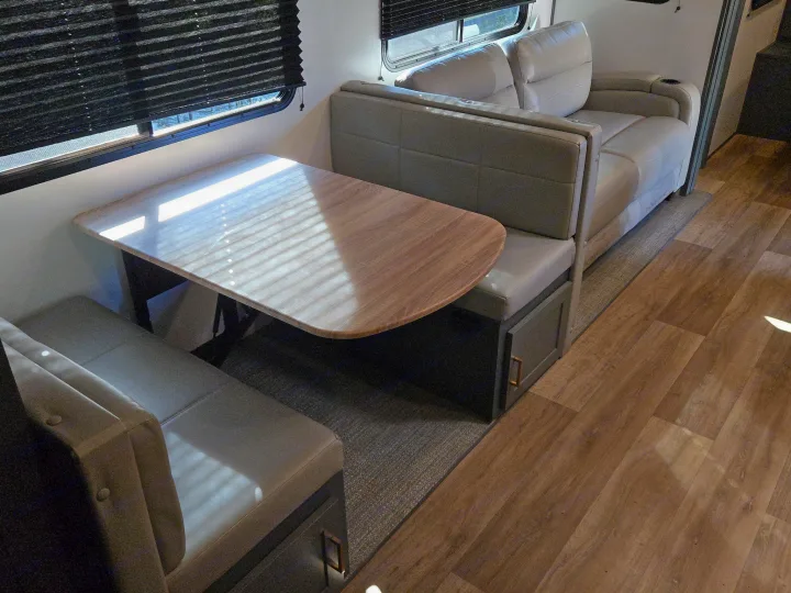 Inside an RV rental: a comfortable dinette with a table and bench seating, plus a relaxed sofa. Sunlight fills the space.. Keystone Bullet 2022
