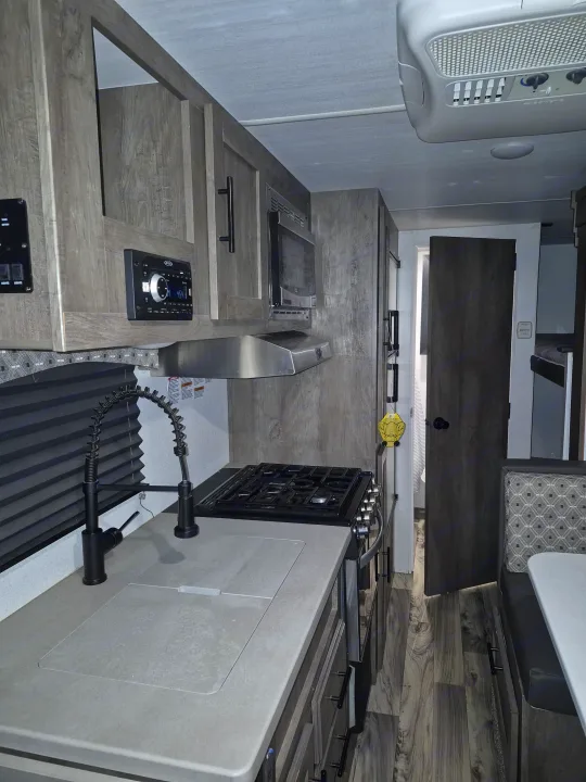 Experience comfort in this RV rental's kitchen. Features a modern sink, stove, microwave, AC, and a dinette next to bunk beds.. Forest River Sonoma 2020