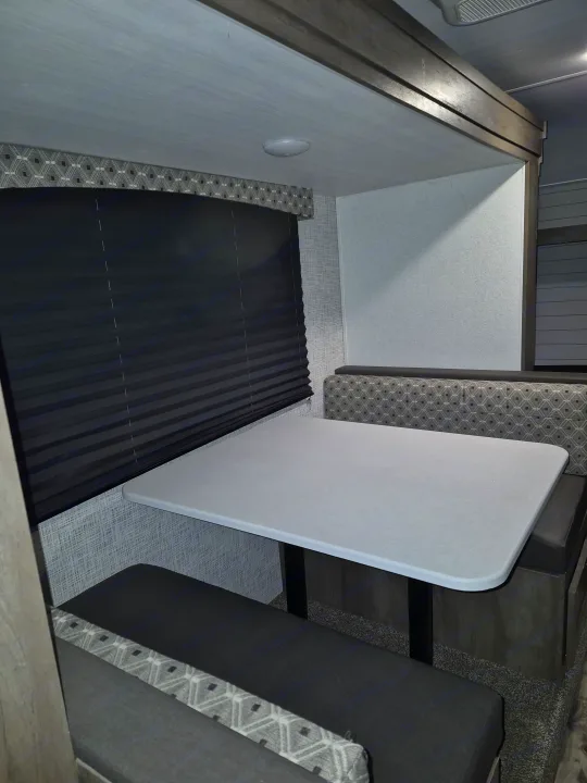 Modern RV rental dinette with sleek table, comfy patterned benches, and a dark window blind, perfect for dining.. Forest River Sonoma 2020