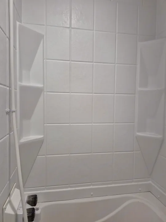 Inside a clean RV rental bathroom: a white shower/tub with built-in corner shelves, a flexible showerhead, and controls.. Forest River Sonoma 2020