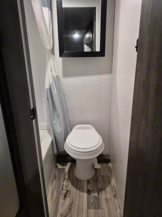 RV rental bathroom: compact space with white toilet, striped shower curtain over tub, and framed mirror.. Forest River Sonoma 2020
