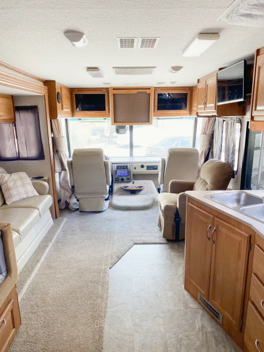 Interior of a spacious RV rental showing the living area, kitchen, and cockpit with light carpet, tile floor, and wood cabinets.. Fleetwood Fiesta LX 2008