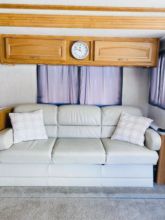 Light sofa with plaid pillows, wood cabinetry with an analog clock, and curtains in a comfortable RV rental interior.. Fleetwood Fiesta LX 2008