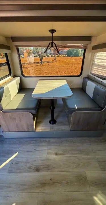 Interior of an rv rental showing a bright dinette area with two gray upholstered bench seats, a light table, and a scenic window.. Forest River Surveyor 2022