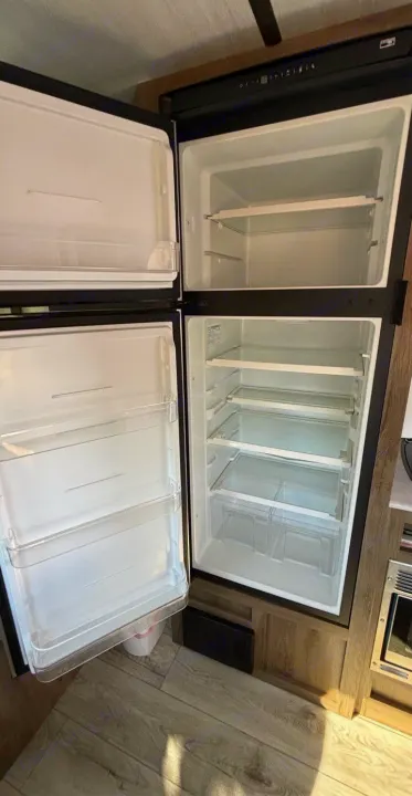 An open, spotless RV rental refrigerator/freezer, with shelves and door bins, ready for your groceries on an adventure.. Forest River Surveyor 2022