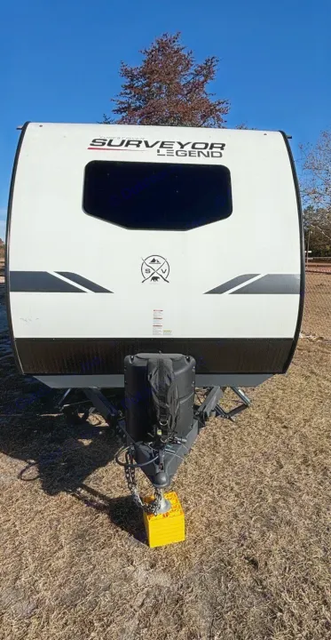 A white Surveyor Legend travel trailer, perfect for your next rv rental, features a front hitch on yellow leveling blocks on dry ground.. Forest River Surveyor 2022
