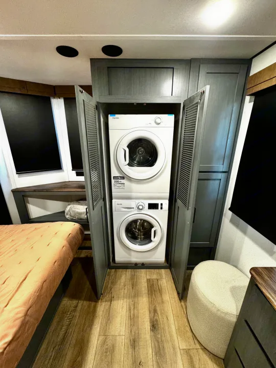 Inside an RV rental, a stackable washer and dryer unit, with a bed and cozy seating visible.. Forest River Puma Destination 2026