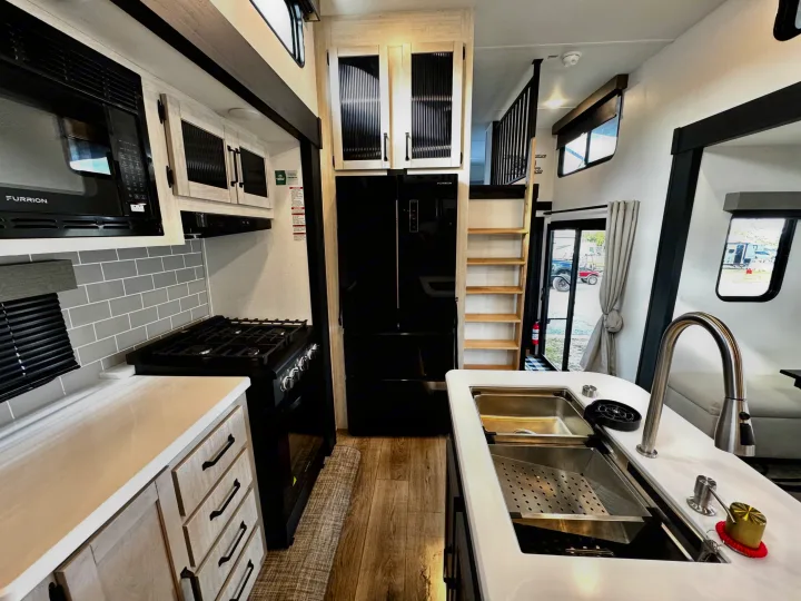 Modern RV rental kitchen with black appliances, light wood cabinets, and a convenient sink, ready for travel.. Forest River Puma Destination 2026